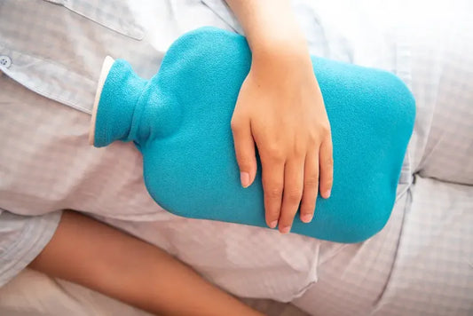 Schwangere wärmt sich Bauch mit Wärmflasche.
