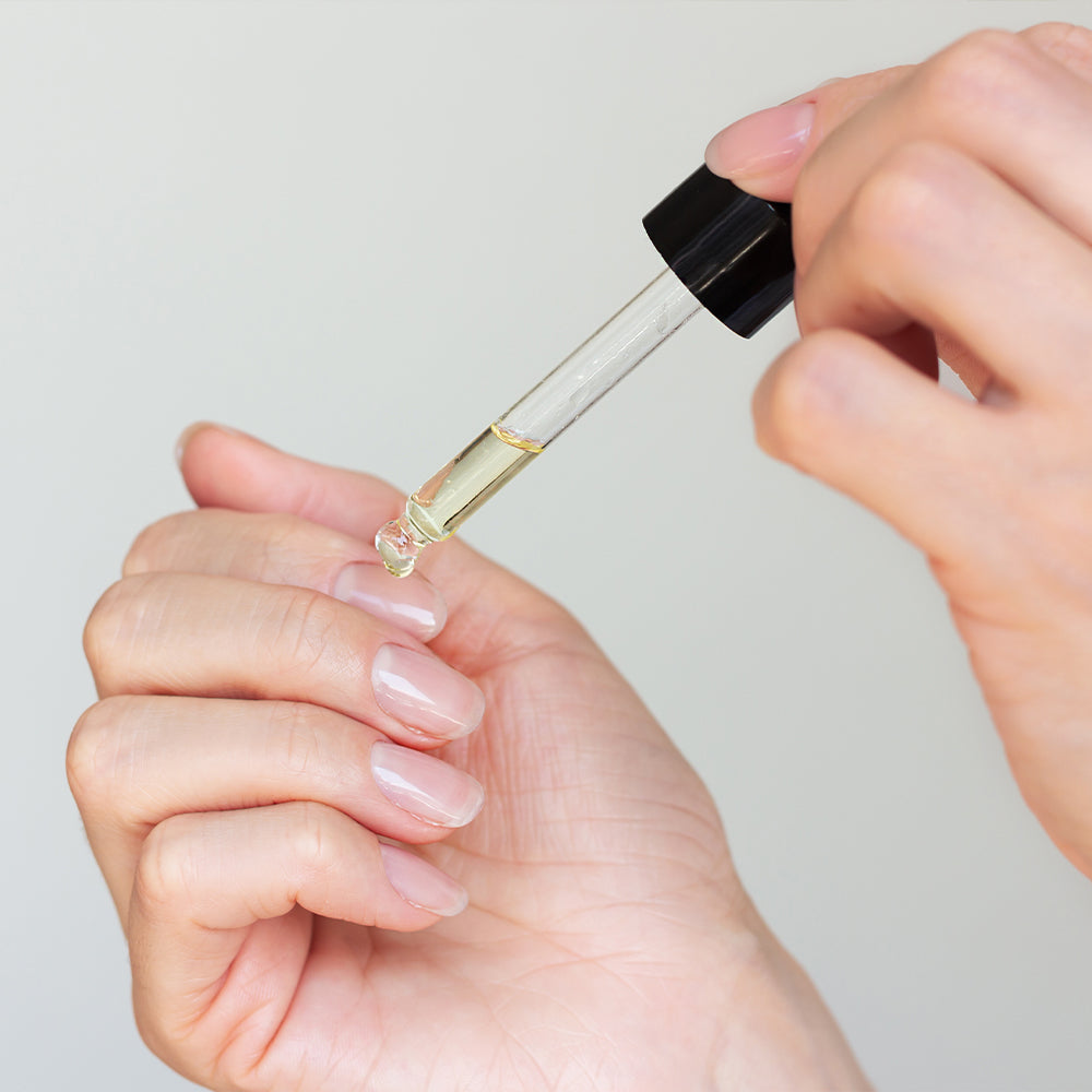 Teebaumöl mit Pipette: Hand tropft Öl auf die Fingerspitzen